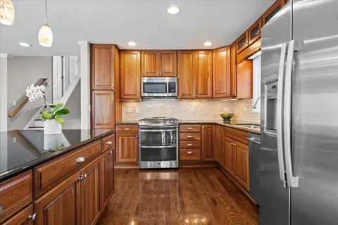 a kitchen with stainless steel appliances granite countertop a refrigerator a sink dishwasher a oven with wooden cabinets and floor