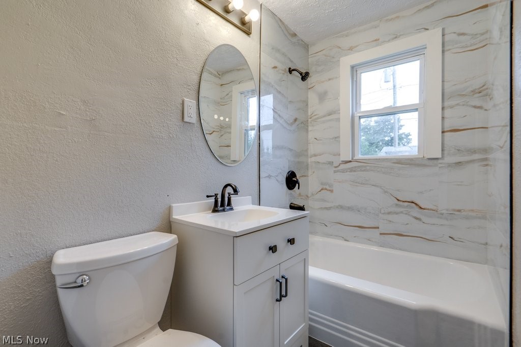 396 Niagara Road Vermilion, OH 44089 - Photo 13 of 15 Bathroom featuring a white vanity with black hardware, a round mirror, a white toilet, and a tiled shower/tub combination with a window