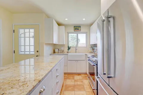 a kitchen with stainless steel appliances kitchen island granite countertop a sink dishwasher stove and white cabinets with wooden floor