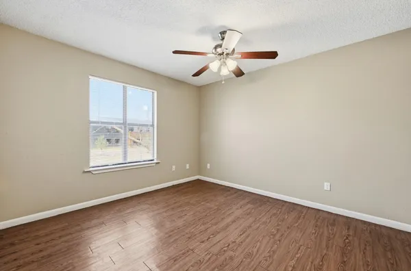 an empty room with wooden floor fan and windows