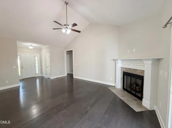 a view of an empty room with wooden floor fireplace and a window