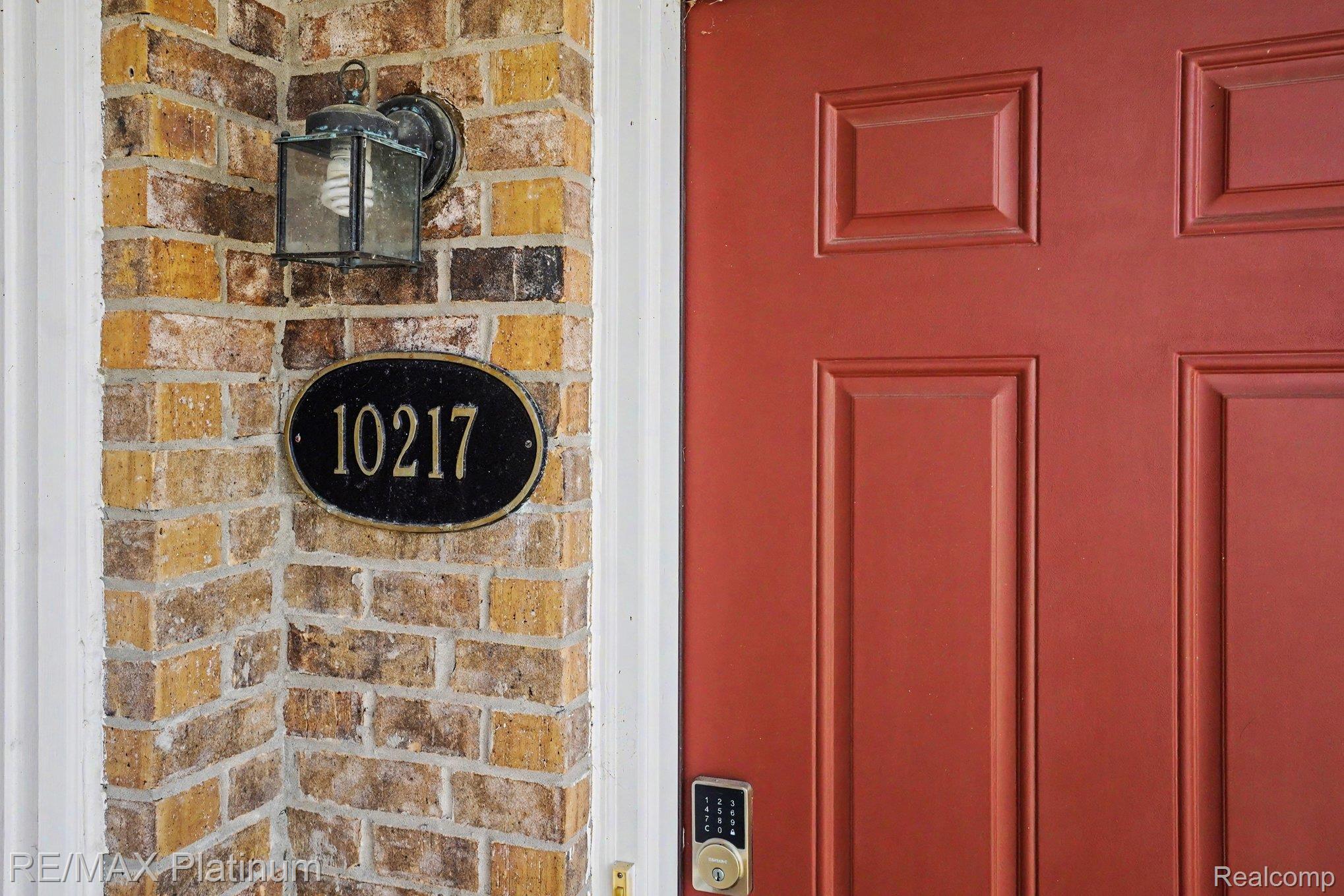 10217 Crossview Trail Howell, MI 48855 - Photo 5 of 26 Brick exterior featuring a paneled red entry door with digital keypad entry