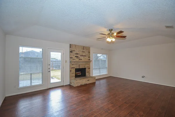 an empty room with wooden floor fireplace and windows