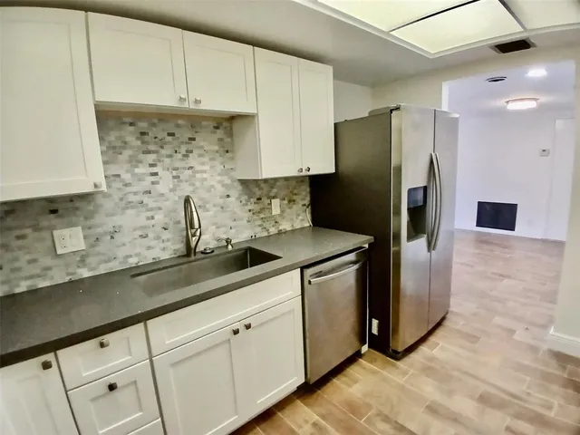 a kitchen with stainless steel appliances granite countertop a refrigerator a sink and white cabinets