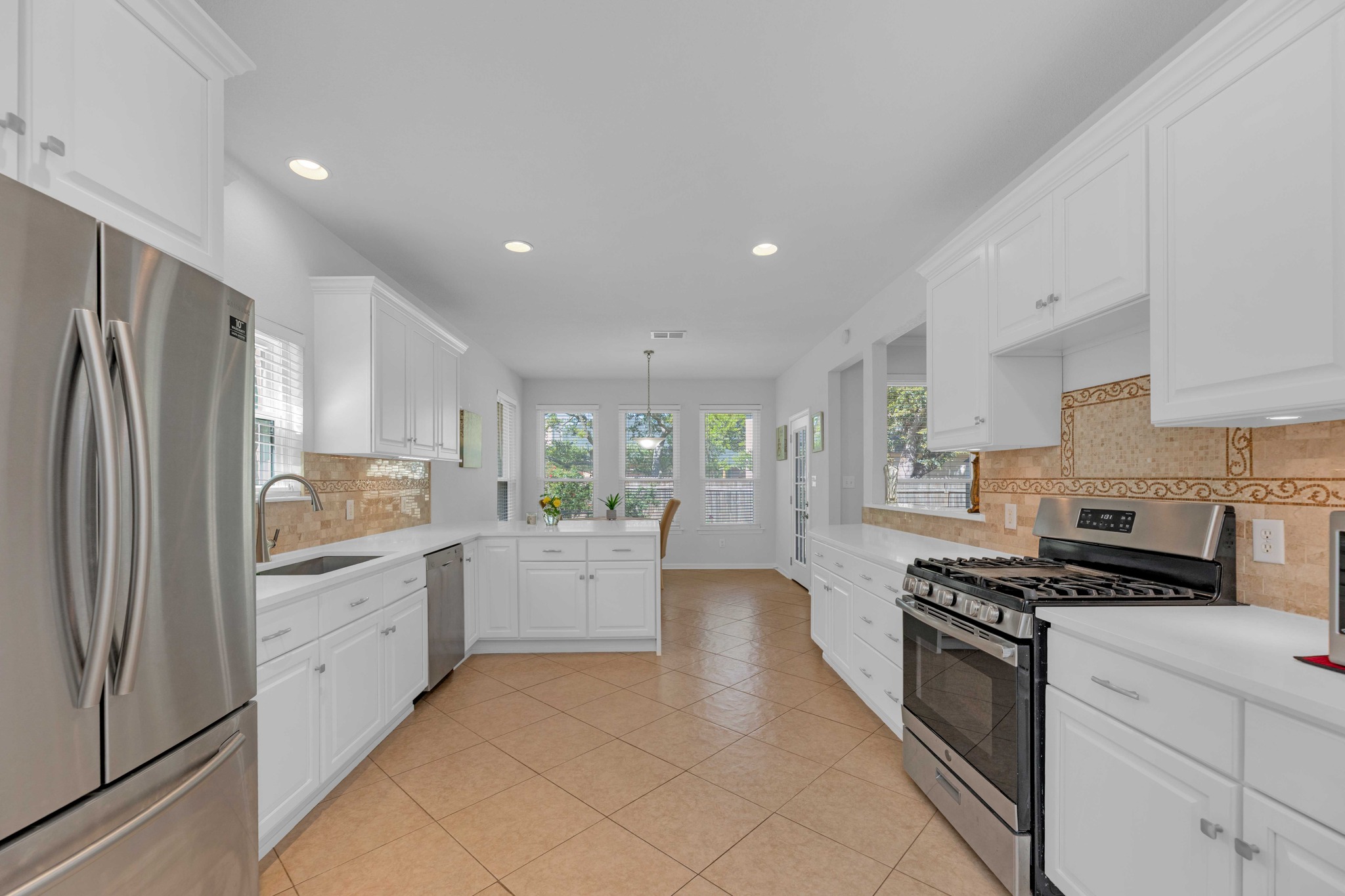 12528 Labrador Cove Austin, TX 78729 - Photo 14 of 40 Kitchen: Expansive and light filled with quartz countertops, white cabinetry, stainless steel appliances, and a gas range. Generous prep space and storage flow into the breakfast area, creating a functional layout ideal for everyday living and entertaining.