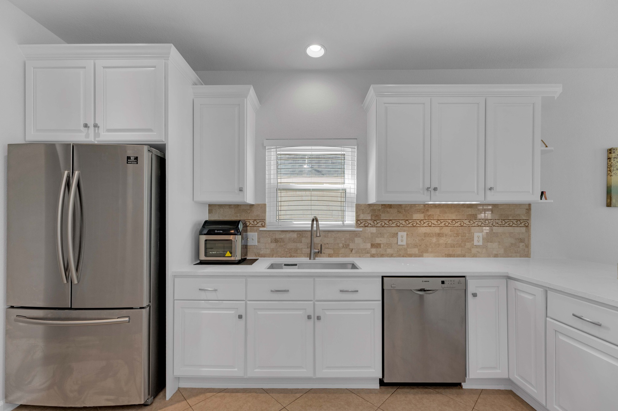 12528 Labrador Cove Austin, TX 78729 - Photo 15 of 40 Kitchen Detail: Clean and modern design with quartz countertops, white cabinetry, and stainless steel appliances. Window over the sink brings in natural light, complemented by a stylish tile backsplash and functional workspace.