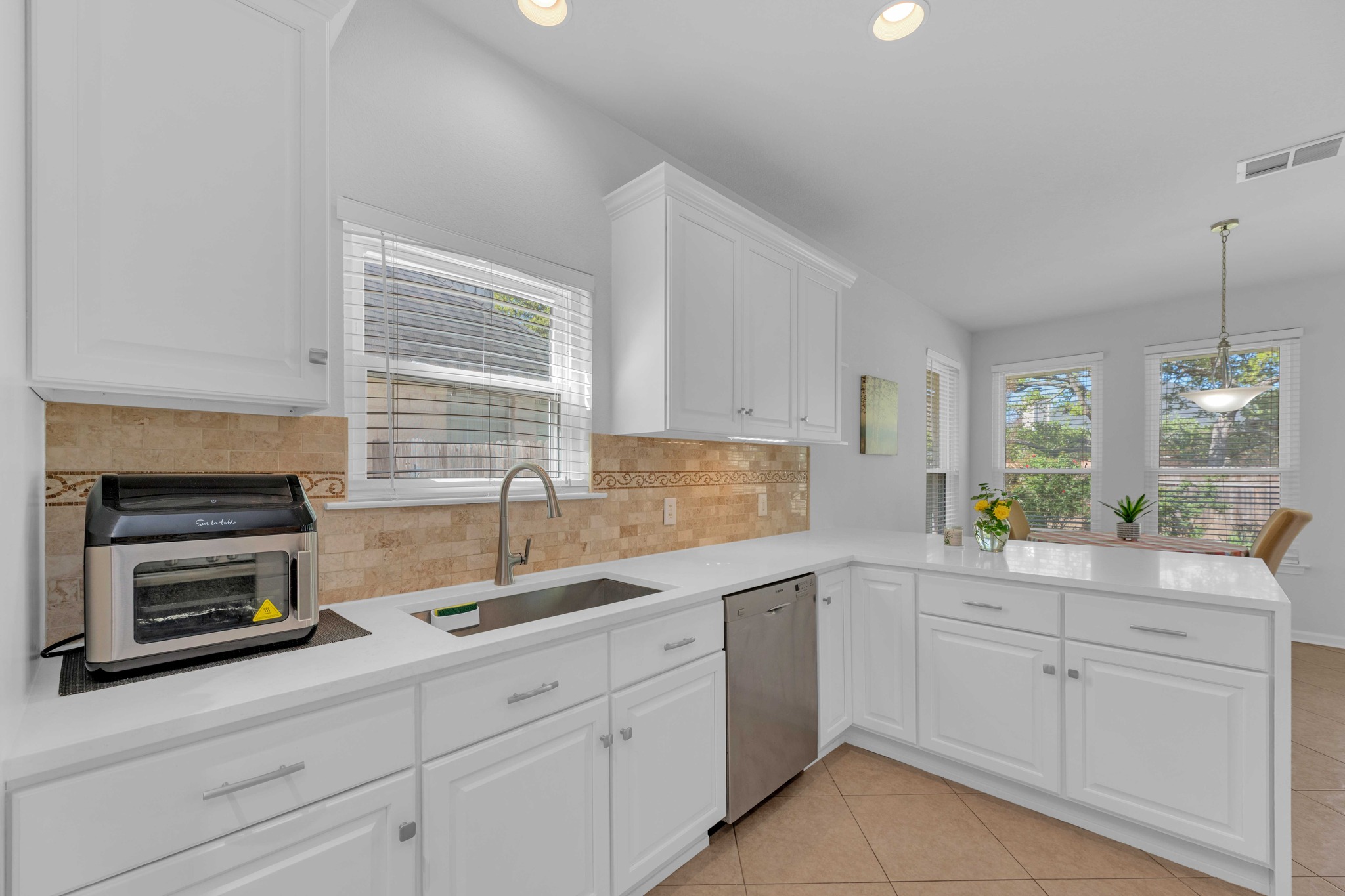 12528 Labrador Cove Austin, TX 78729 - Photo 16 of 40 Kitchen Detail: Bright and functional workspace with quartz countertops, white cabinetry, and stainless steel sink. Window over the sink brings in natural light, with a stylish tile backsplash and open flow to the breakfast area.