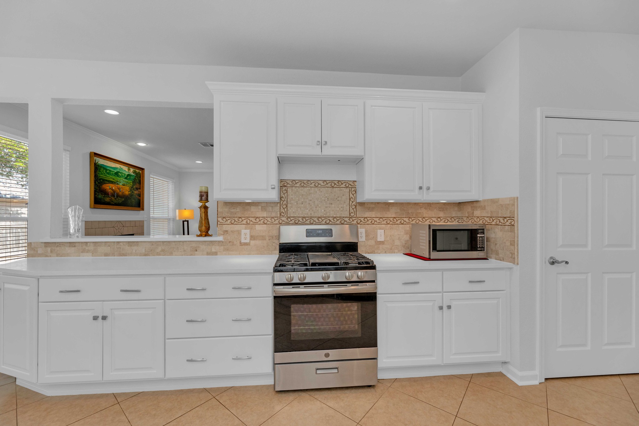 12528 Labrador Cove Austin, TX 78729 - Photo 17 of 40 Kitchen Detail: Well designed cooking area with gas range, quartz countertops, and extensive white cabinetry. Stylish tile backsplash and open sightline to the living area enhance both function and flow.