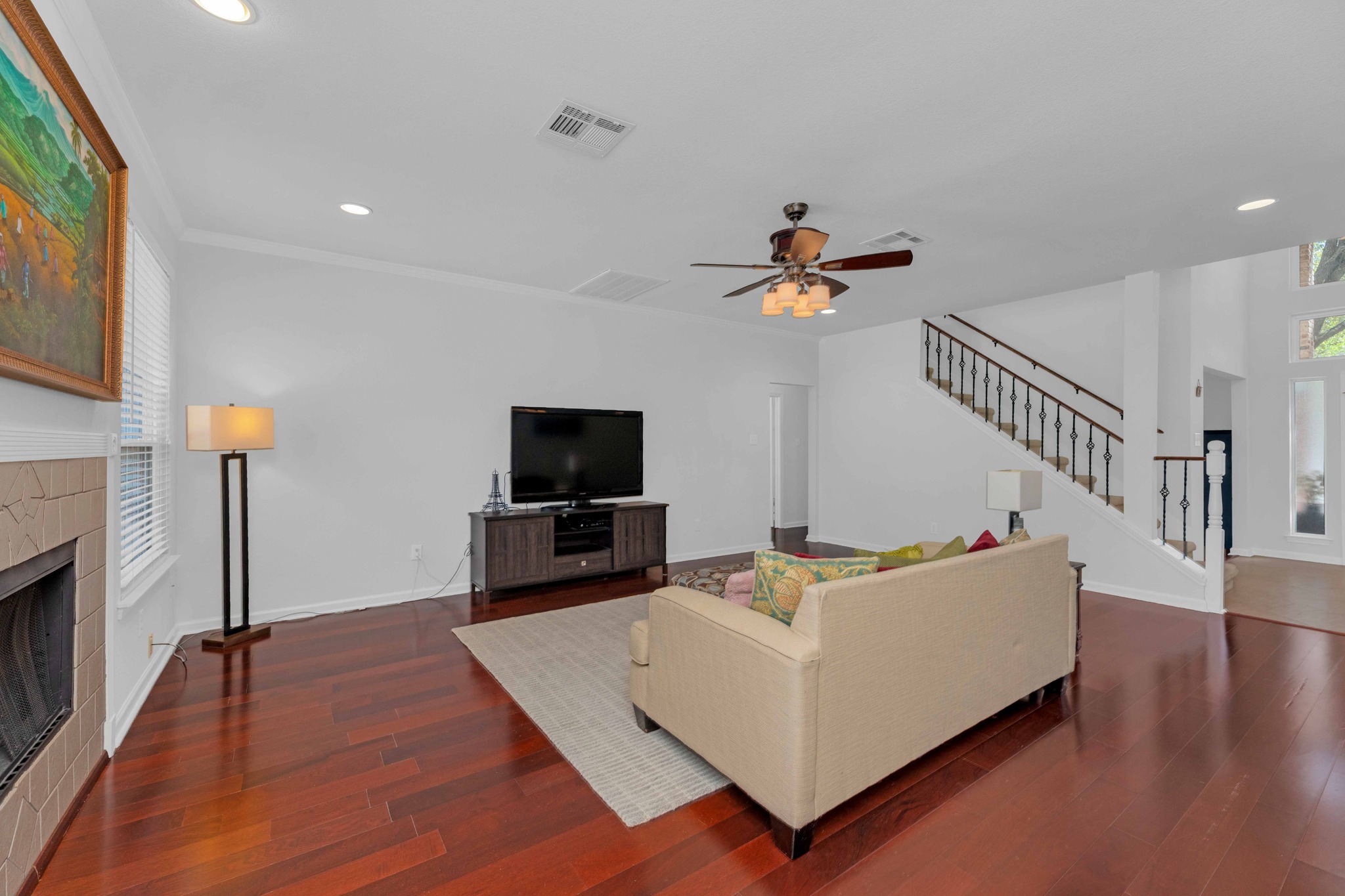 12528 Labrador Cove Austin, TX 78729 - Photo 6 of 40 Family Room: Spacious and open living area with rich wood flooring, a fireplace focal point, and abundant natural light. Seamlessly connected to the entry and staircase with wrought iron railings, creating a comfortable space for everyday living and entertaining.