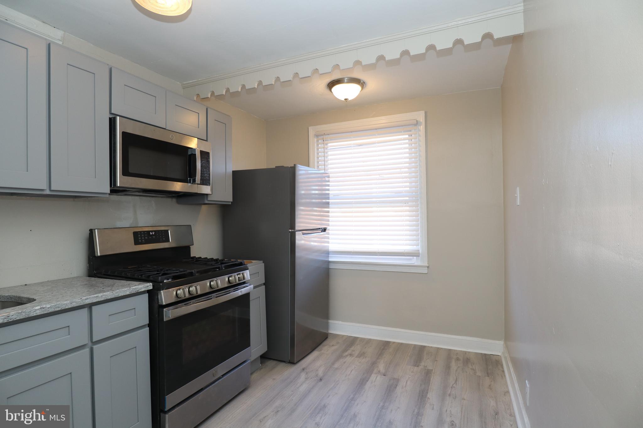 6335 Carnation Street, Unit 2 Philadelphia, PA 19144 - Photo 13 of 35 a kitchen with granite countertop a stove a microwave and wooden floor