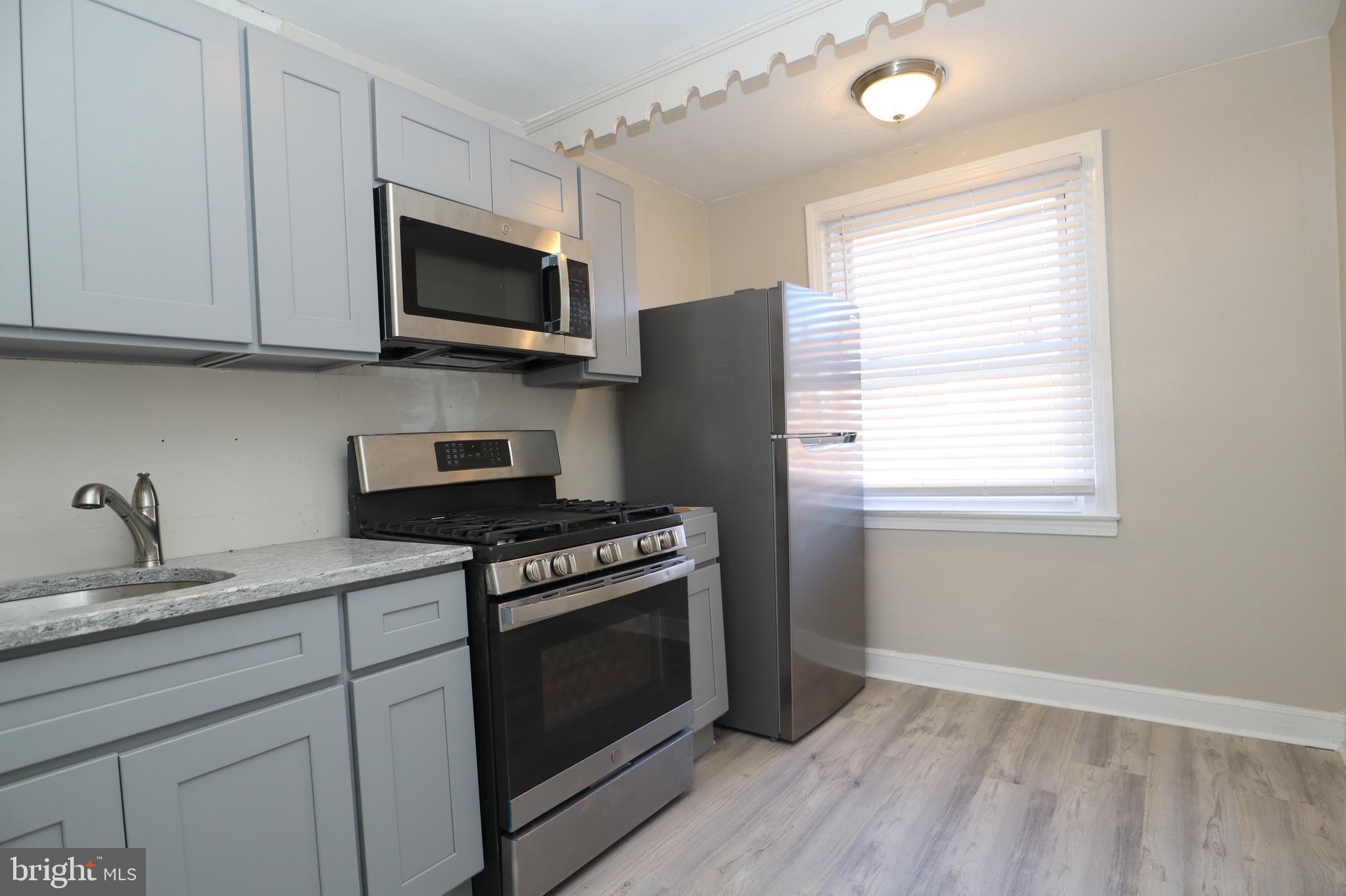 6335 Carnation Street, Unit 2 Philadelphia, PA 19144 - Photo 31 of 35 a kitchen with stainless steel appliances granite countertop a stove a microwave and a white cabinets