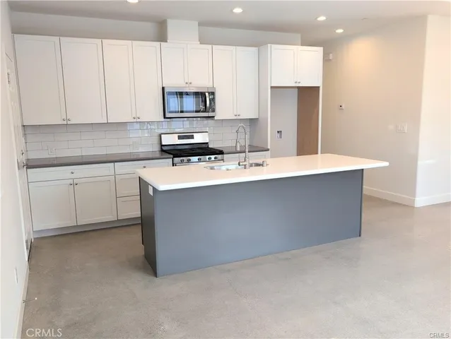 a kitchen with stainless steel appliances a sink a stove a microwave a refrigerator a white cabinets and a counter top