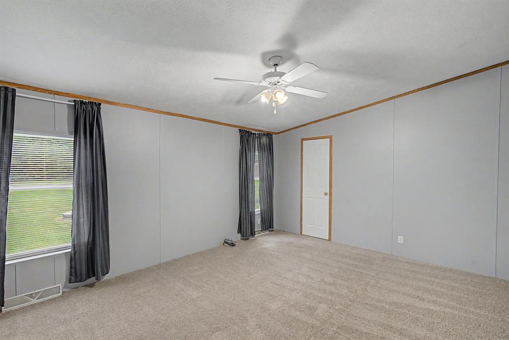1202 Princeton Road Princeton, LA 71067 - Photo 13 of 19 Spacious room featuring light gray walls, plush carpeting, a ceiling fan with integrated lighting, and two windows providing natural light