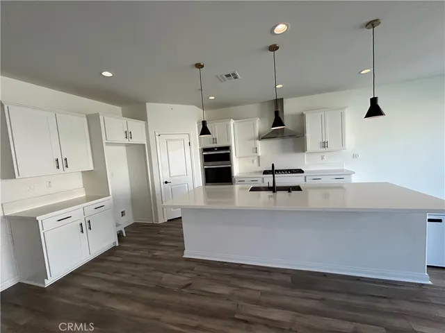 a large kitchen with stainless steel appliances kitchen island granite countertop a stove a sink a refrigerator and white cabinets with wooden floor