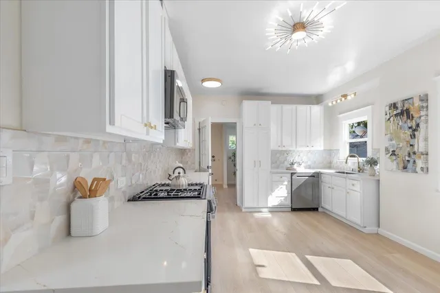 a kitchen with stainless steel appliances granite countertop a refrigerator a stove a sink and white cabinets with wooden floor