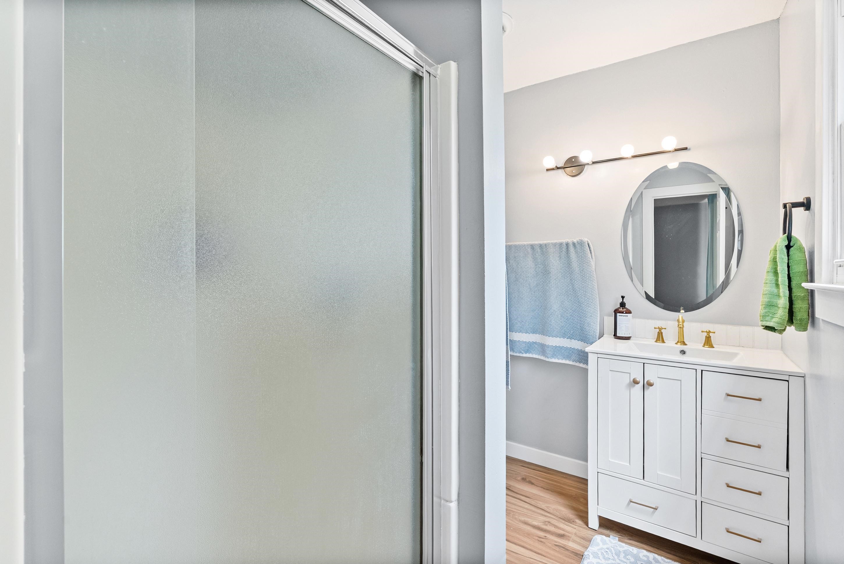 779 Strickland Road Coldwater, MS 38618 - Photo 30 of 40 White shaker vanity with gold-tone hardware, rectangular undermount sink, oval-framed mirror, four-bulb vanity light, and wood-finish flooring