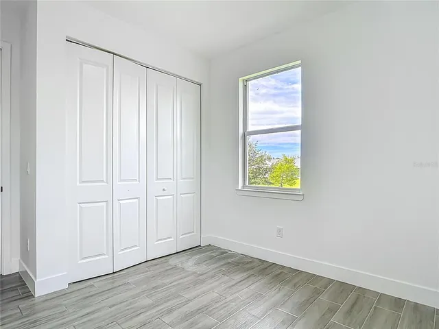 an empty room with wooden floor closet and windows