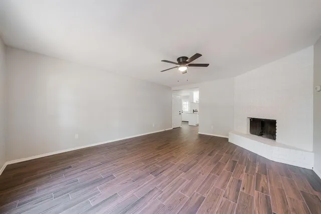 a view of an empty room with wooden floor and a ceiling fan