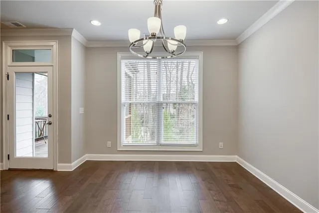 an empty room with wooden floor chandelier and windows