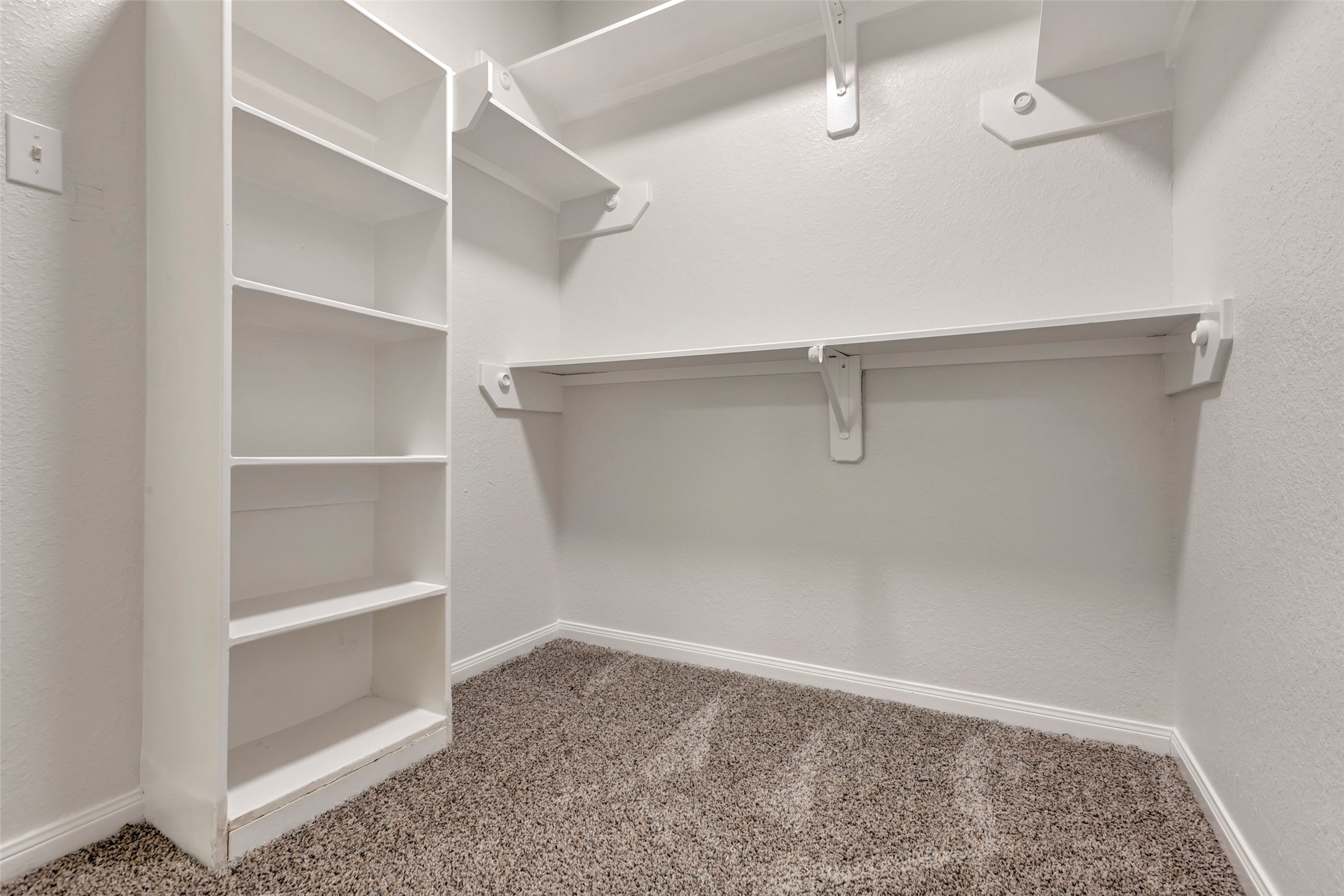 770 Hunt Road, Unit 212 Baytown, TX 77521 - Photo 29 of 40 This is a clean and compact walk-in closet featuring built-in shelves on one side and a hanging rod with a shelf above it for additional storage. The space is carpeted and well-lit, offering a practical solution for clothing and accessory organization.