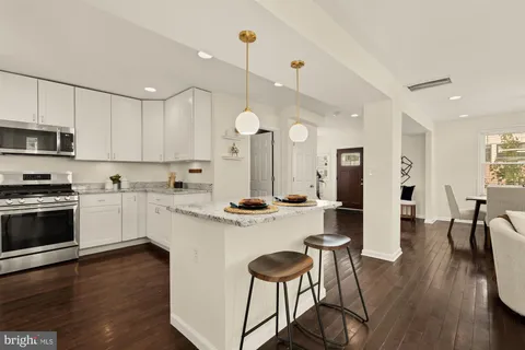 a kitchen with stainless steel appliances kitchen island granite countertop a stove a sink a refrigerator and a dining table with wooden floor