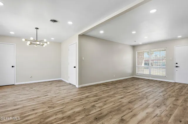 a view of an empty room with wooden floor kitchen view and a window