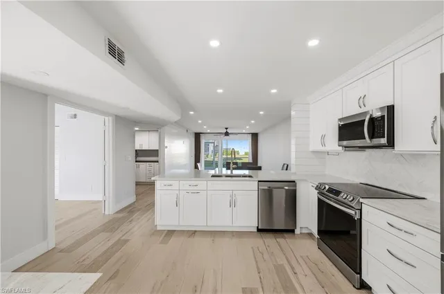 a kitchen with stainless steel appliances a stove top oven a sink a refrigerator white cabinets and wooden floor