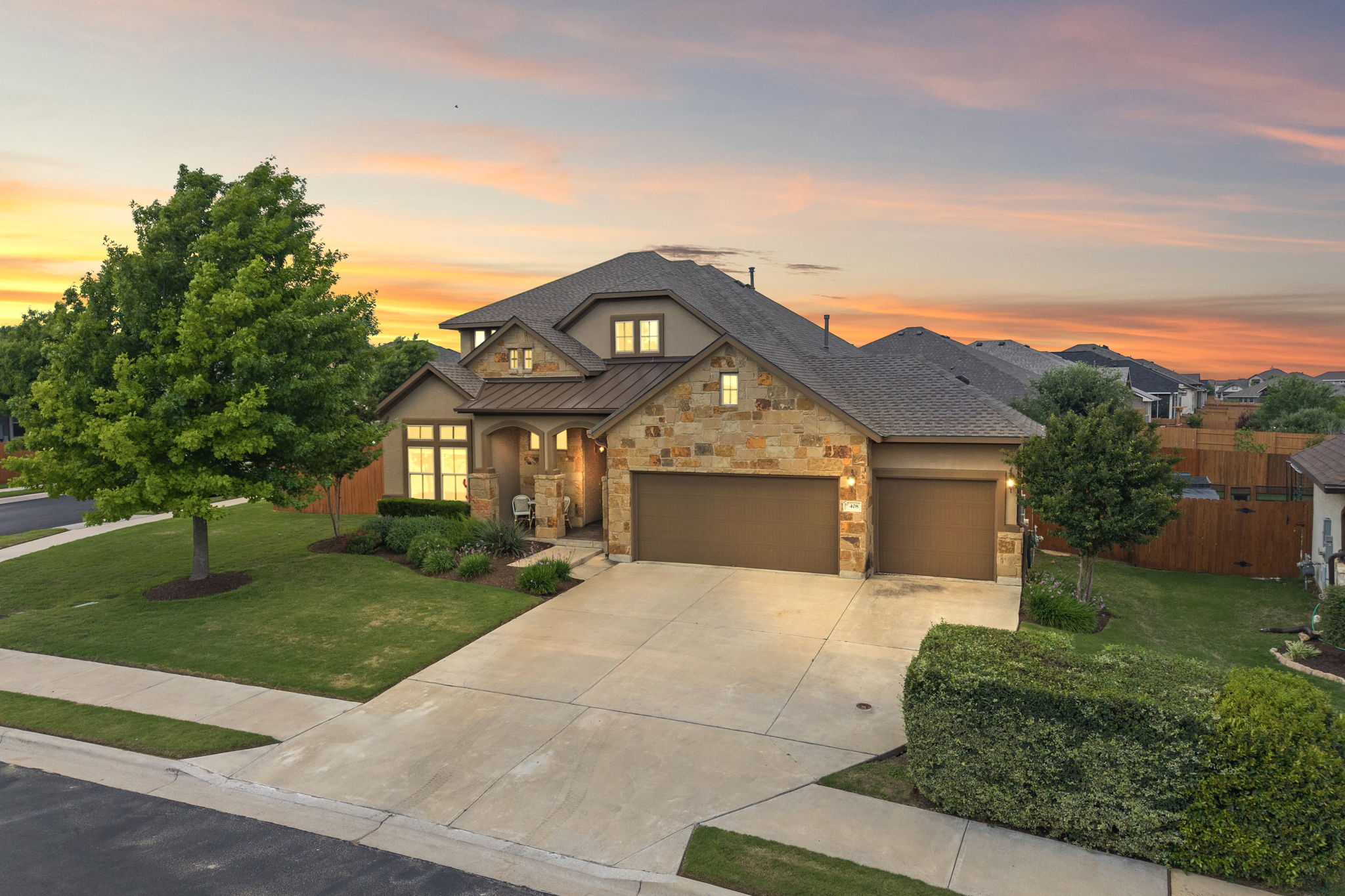 This property features a stone and stucco exterior, a two-car garage, and a well-maintained front lawn with mature trees and shrubs