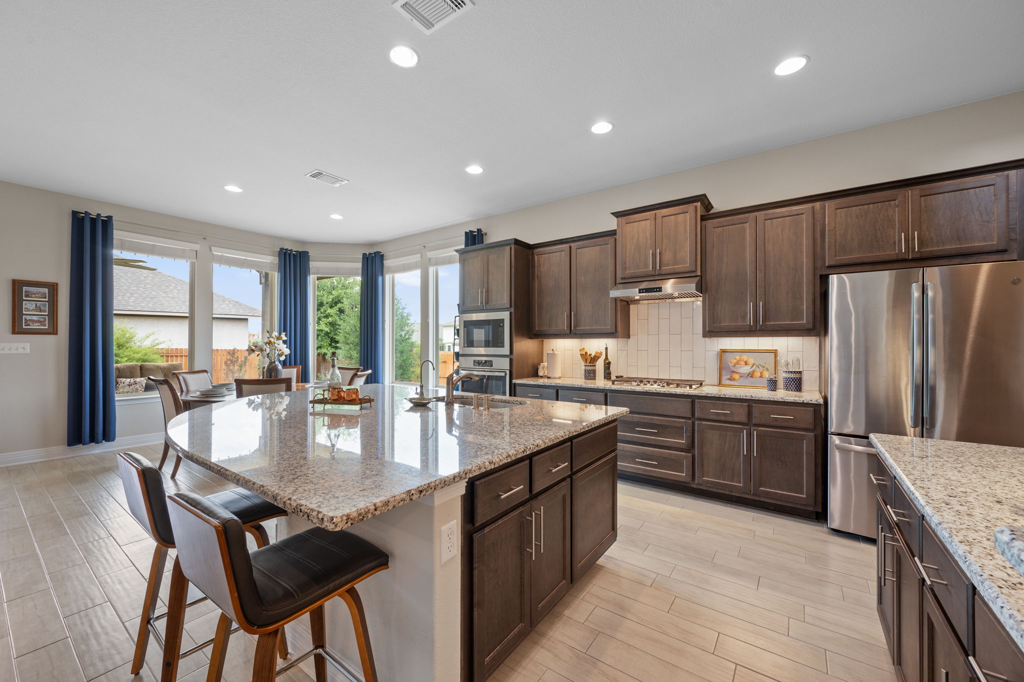 408 Bell Boot Pass Georgetown, TX 78626 - Photo 11 of 40 Spacious kitchen featuring an expansive center island with seating, dark wood cabinetry, light granite countertops, stainless steel appliances, and light wood-look tile flooring