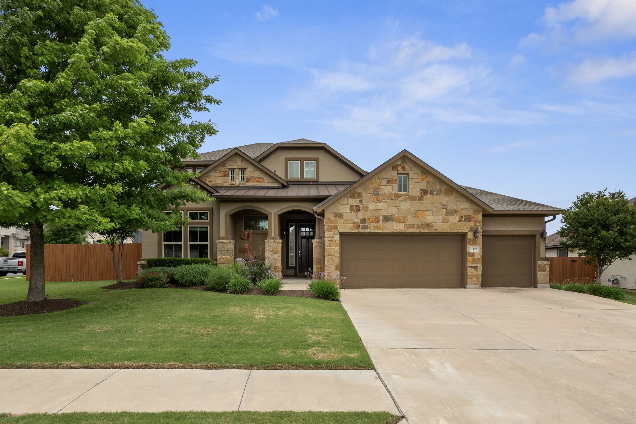 408 Bell Boot Pass Georgetown, TX 78626 - Photo 2 of 40 The property features a stone and stucco exterior, a manicured front lawn, and a wide concrete driveway leading to two separate garage doors