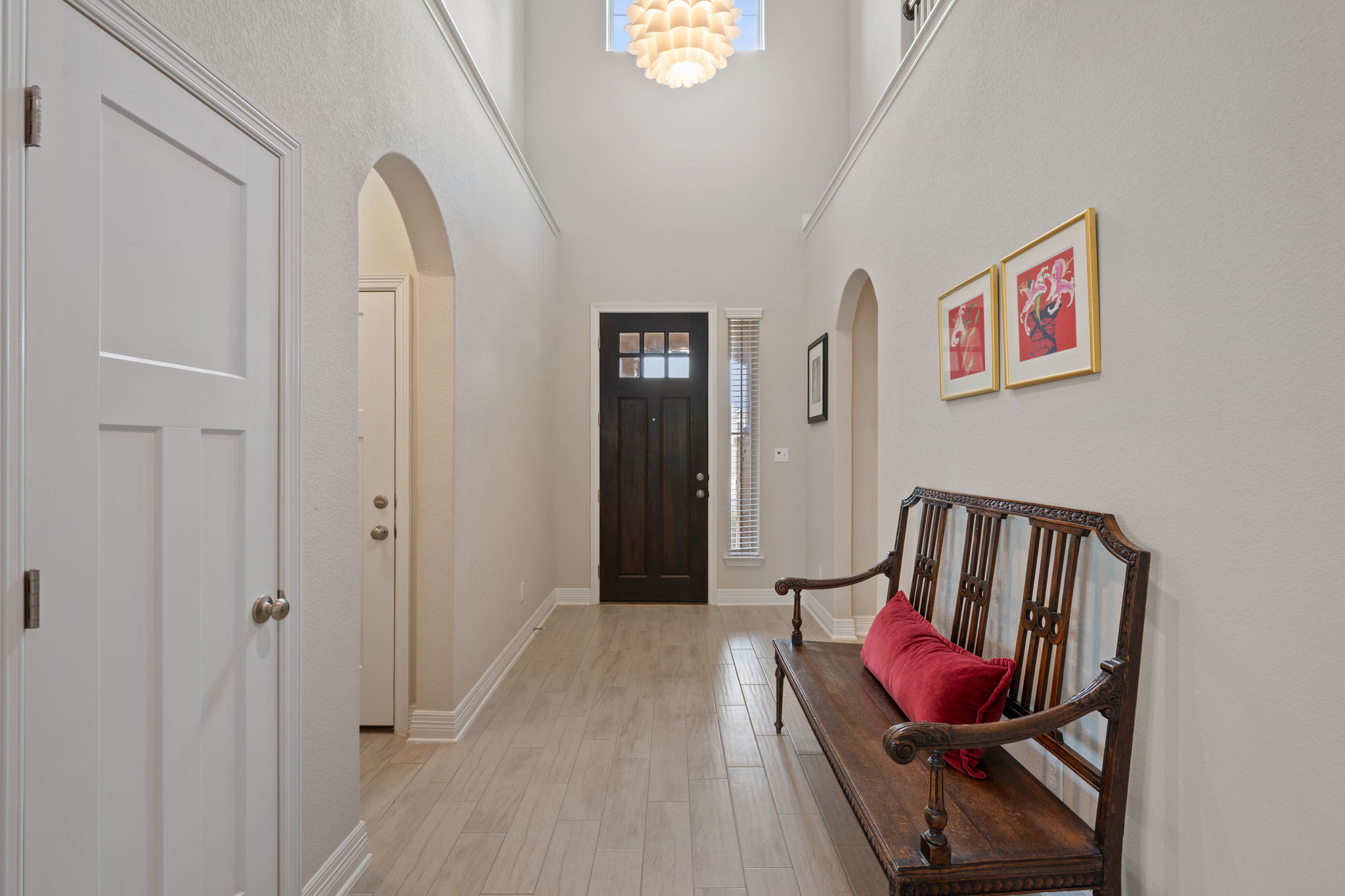 408 Bell Boot Pass Georgetown, TX 78626 - Photo 21 of 40 Entryway featuring light wood-finish flooring, a dark paneled front door with multiple glass panes, high ceilings, arched doorways, and a prominent chandelier