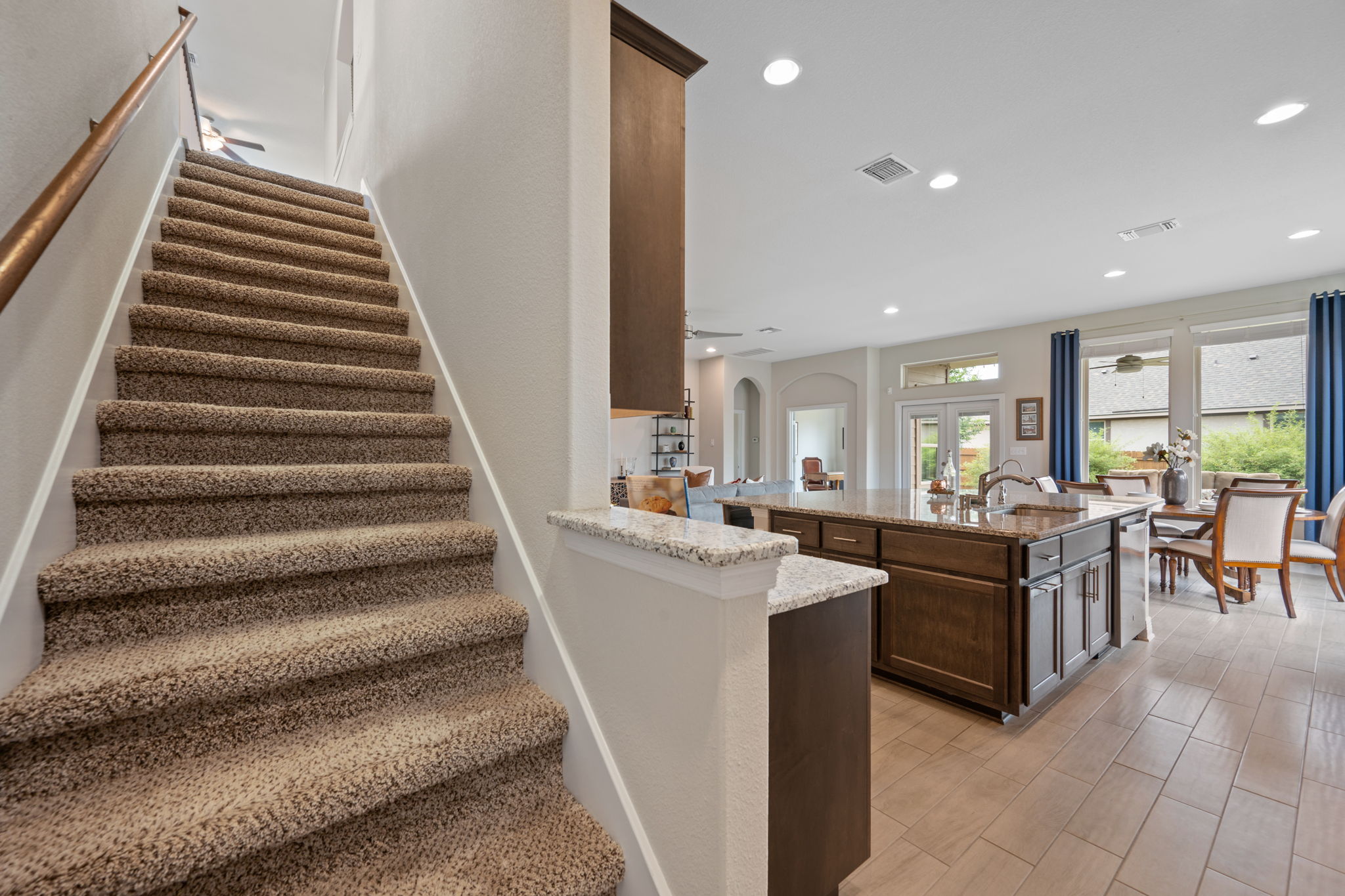 408 Bell Boot Pass Georgetown, TX 78626 - Photo 25 of 40 Carpeted staircase featuring a wood handrail, alongside a kitchen island with granite countertops and dark wood cabinetry, and tiled flooring