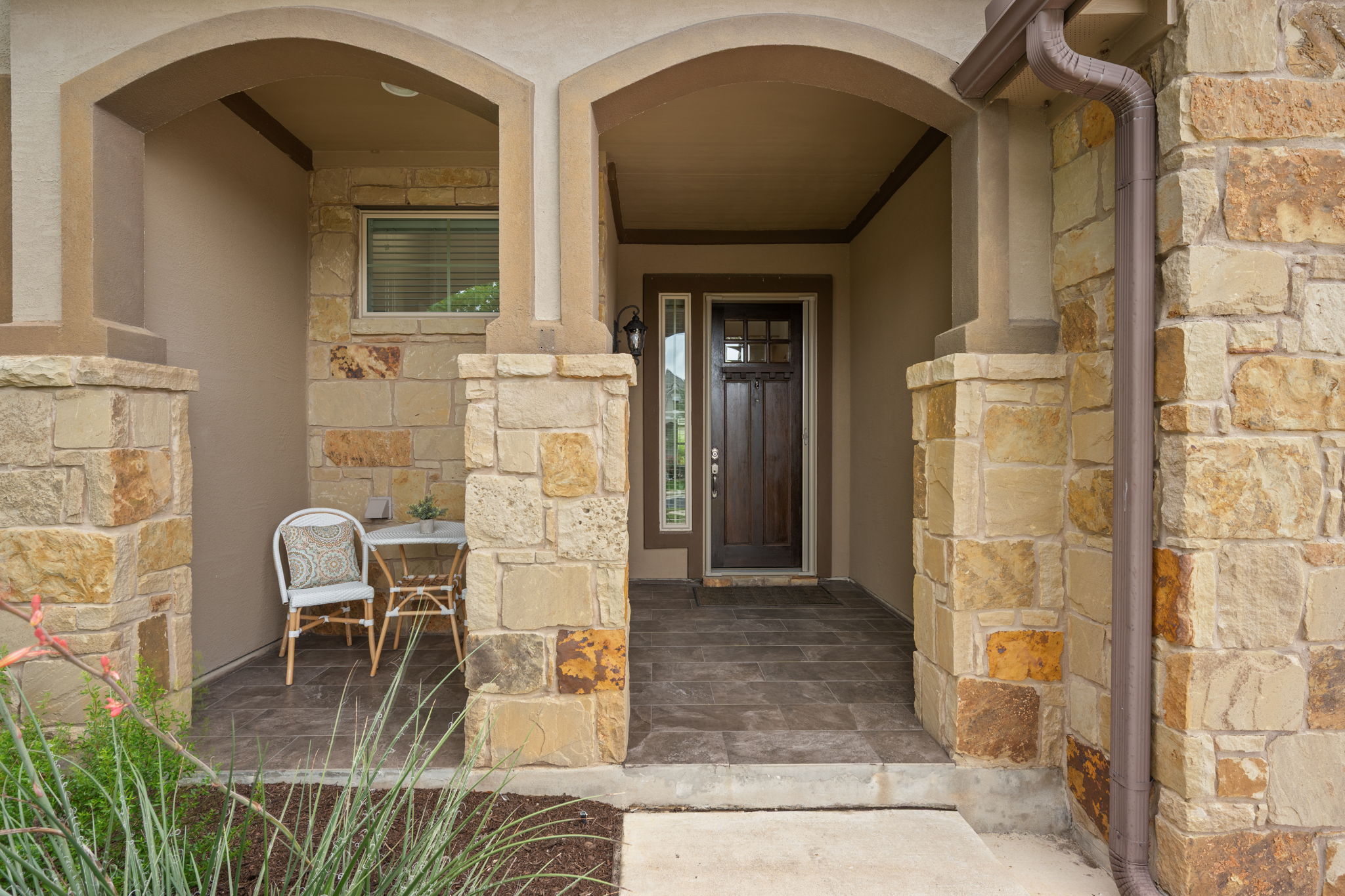 408 Bell Boot Pass Georgetown, TX 78626 - Photo 3 of 40 The property features an inviting stone facade with arched entryways, a dark wood front door with glass inserts, and a covered porch area with tiled flooring