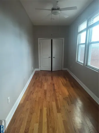 an empty room with wooden floor chandelier fan and windows