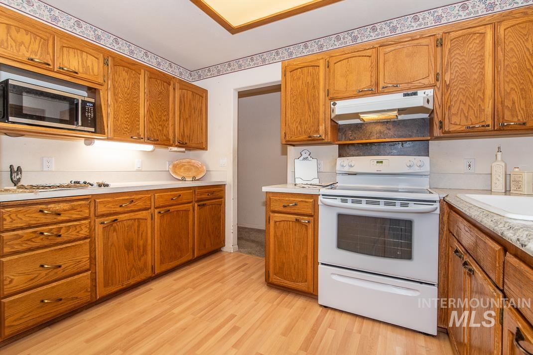 16517 Madison Road Nampa, ID 83687 - Photo 6 of 26 Kitchen with white electric stove, light countertops, brown cabinetry, and under cabinet range hood