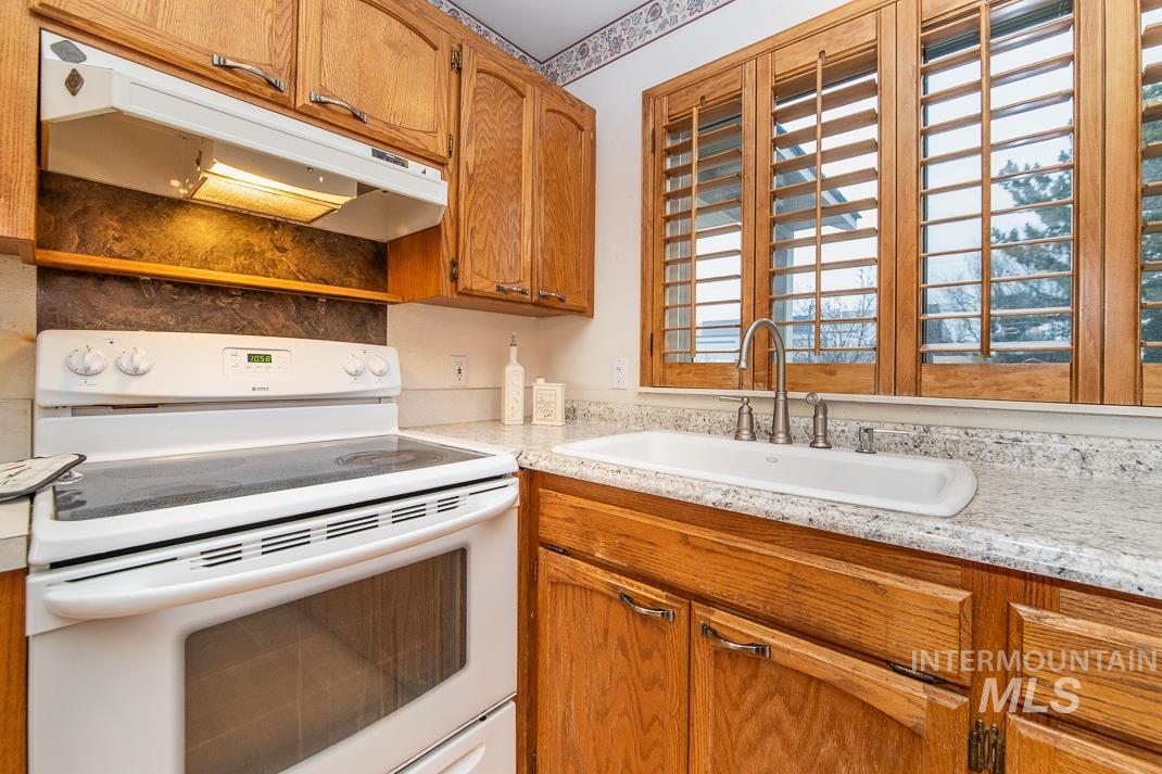 16517 Madison Road Nampa, ID 83687 - Photo 8 of 26 Kitchen with white range with electric cooktop, brown cabinetry, and under cabinet range hood