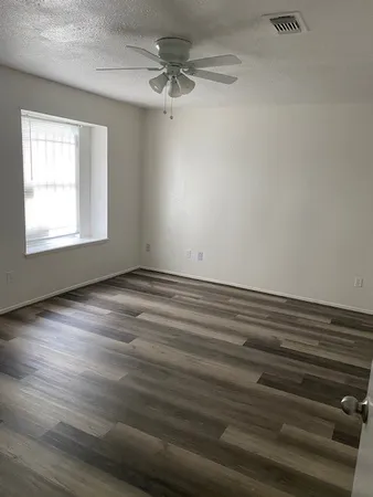 an empty room with wooden floor fan and windows