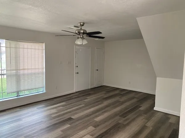 an empty room with wooden floor fan and windows