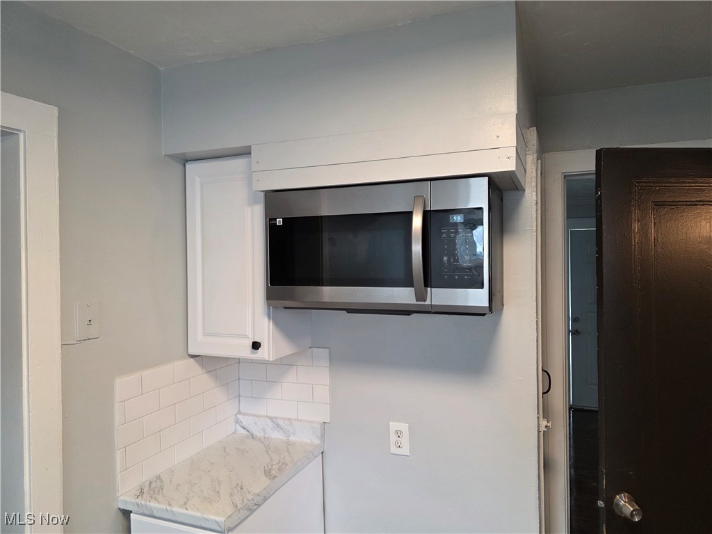 991 Helmsdale Road Cleveland, OH 44112 - Photo 10 of 39 Kitchen view of decorative backsplash, stainless steel microwave, white cabinetry, and light stone counters