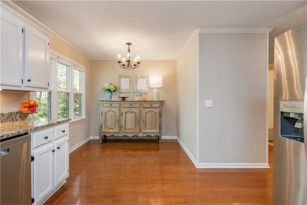 a kitchen with granite countertop a refrigerator a stove a oven and white cabinets with wooden floor