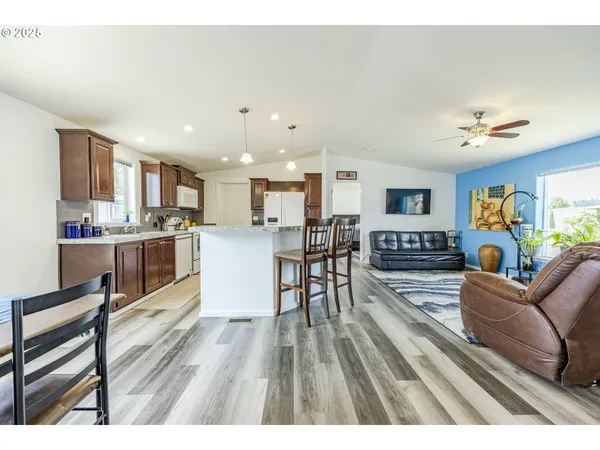 a living room with stainless steel appliances furniture wooden floor and a kitchen view