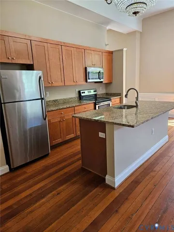 a kitchen with stainless steel appliances granite countertop a sink a stove a refrigerator and island with wooden floors