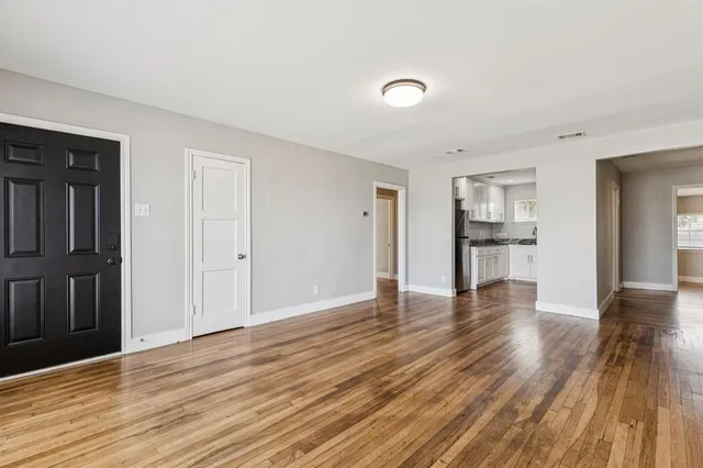 a view of empty room with wooden floor and kitchen