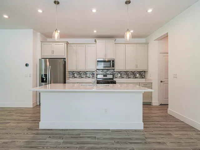 a large kitchen with stainless steel appliances granite countertop a stove a sink a refrigerator and white cabinets with wooden floor