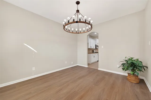 an empty room with wooden floor chandelier fan and windows
