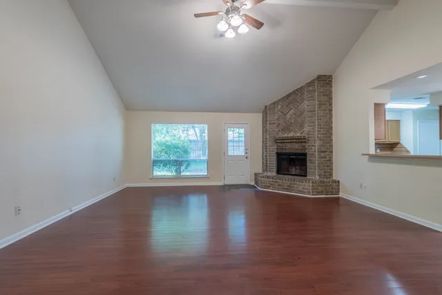 an empty room with wooden floor fireplace and windows