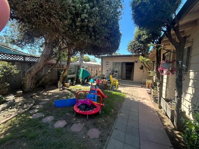 a view of a backyard with table and chairs potted plants and a large tree