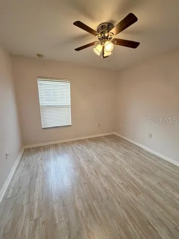 an empty room with wooden floor fan and windows