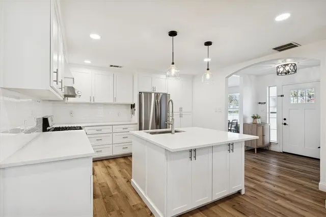 a kitchen with kitchen island a stove a sink a refrigerator and white cabinets with wooden floor