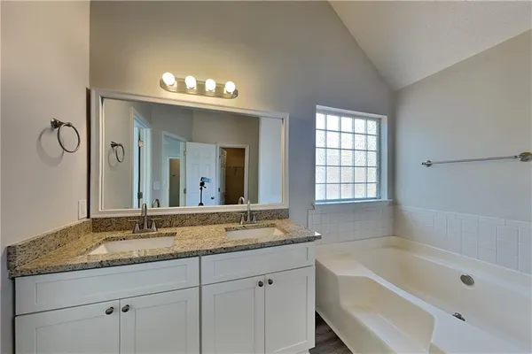 a bathroom with a granite countertop sink a large mirror a bathtub and next to a window